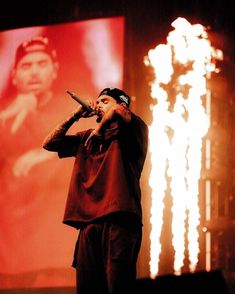 a man standing on top of a stage with a microphone in his hand and fireworks behind him