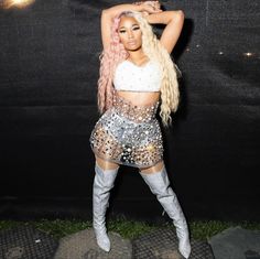 a woman with pink hair and silver boots posing for the camera in front of a black backdrop