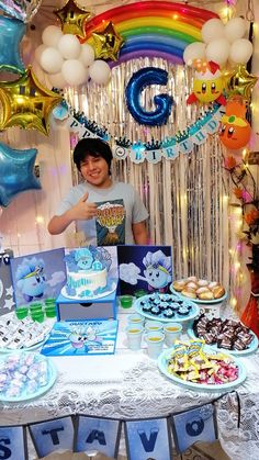 a young boy standing in front of a table filled with cakes and cupcakes