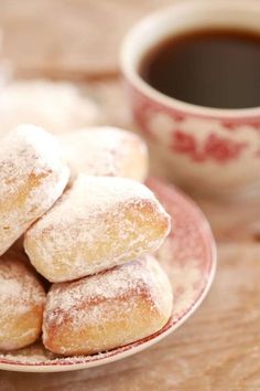 powdered sugar covered doughnuts on a plate next to a cup of coffee