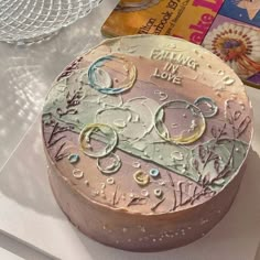 a cake with frosting on it sitting on a table next to a book and glass bowl