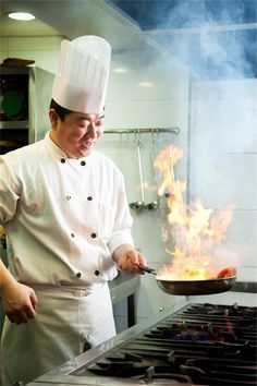 a chef is cooking on the stove with flames coming out of his pan and smiling