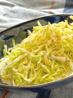 a bowl filled with shredded cabbage on top of a tablecloth next to a fork