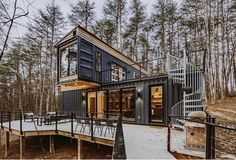 a house made out of shipping containers on a deck in the woods with stairs leading up to it