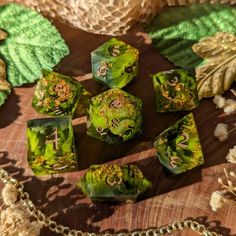 some green and gold dices are on a wooden surface with leaves around them, along with a chain