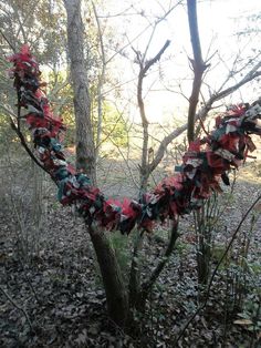 a wreath made out of red, white and blue ribbons hanging from a tree in the woods