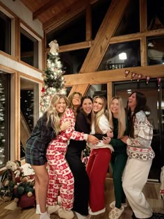 four women in matching pajamas pose for a photo with a christmas tree and lights behind them