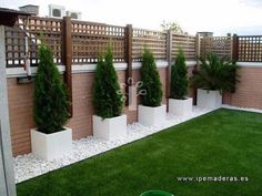 some plants are in large white planters on the grass near a brick wall and fence