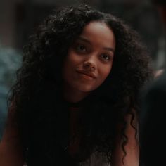 a close up of a person with long curly hair and wearing a white shirt looking at the camera