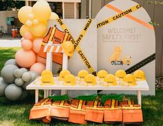 there is a construction themed dessert table on the grass with balloons and caution tape around it