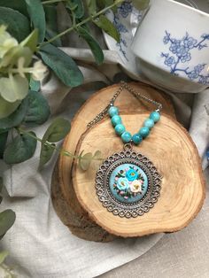 a blue necklace with flowers on it sitting next to a potted plant and cup