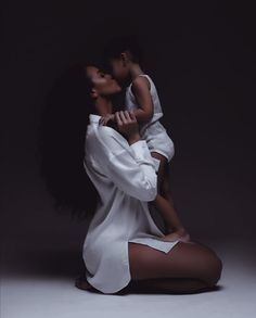 a woman holding a child in her arms while sitting on the floor with dark background