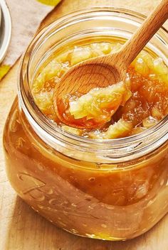 a wooden spoon is in a jar filled with honey and apple jam on a cutting board