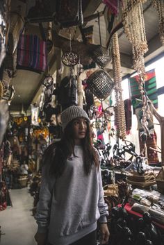 a woman standing in front of a store filled with lots of hats and scarves