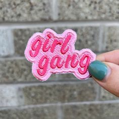 a person holding up a pink sticker with the word girl gang on it in front of a brick wall