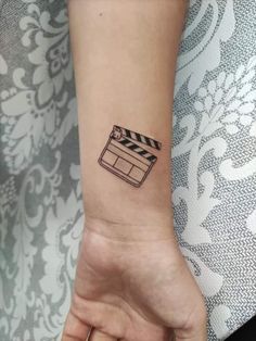 a woman's wrist with a movie clapper tattoo on it