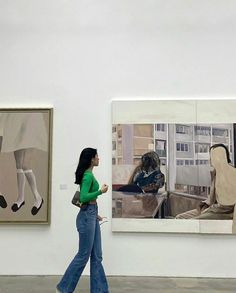 a woman walking past paintings on display in an art gallery