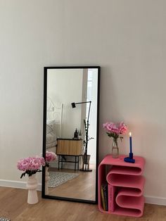 a mirror sitting on top of a wooden floor next to a pink shelf