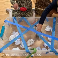 a child is playing with tissue paper and scissors in a plastic container on the floor