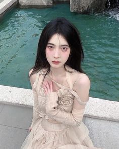 a woman sitting in front of a fountain with her hands on her chest and looking at the camera