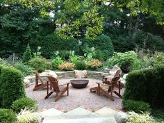 an outdoor seating area with chairs and fire pit surrounded by greenery, shrubs and trees