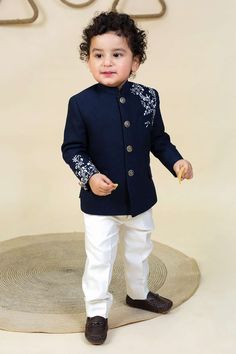 a young boy in a blue jacket and white pants standing on top of a rug