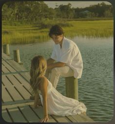 a man and woman sitting on a dock by the water