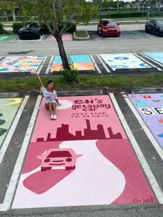 a person sitting on the ground in front of a parking lot with colorful chalk drawings