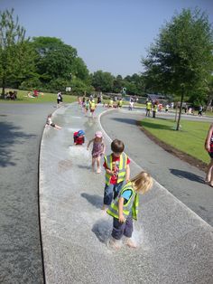 two children are playing in the water at the park while others watch from the side walk