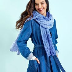 a woman wearing a blue coat and scarf posing for the camera with her hands on her hips