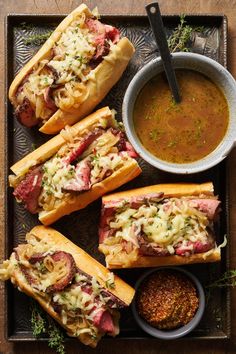 sandwiches with meat, cheese and sauce on a platter next to a bowl of dipping sauce