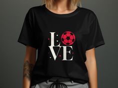 "Show off your passion for soccer and spread the love this Valentine's Day with our unique Soccer Love T-shirt! Perfect for soccer enthusiasts, this shirt features a clever design that spells out LOVE with a soccer ball as the \"O\". The classic black background highlights the red and white graphic, making it an eye-catching choice for match days, casual outings, or as a thoughtful gift for that special someone who lives and breathes the sport. Made with high-quality materials, it's comfortable, durable, and sure to be a hit with soccer fans everywhere. Product Features: Fabrication: 100% Airlume combed and ring-spun cotton, 32 single 4.2 oz. (Ash - 99% Airlume combed and ring-spun cotton, 1% poly) Seams: Side-seamed Fit: Retail Fit Sizing: Unisex Sizing Label: Tear away label" Soccer Heart, Soccer Love, Match Day, Football Love, Sports Tee, Soccer Fans, Sport T-shirts, Couple Matching, Heart Shirt