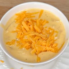 a white bowl filled with cheese soup on top of a wooden table next to a spoon