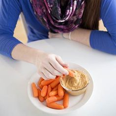 a woman sitting at a table with carrots and hummus