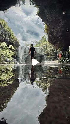 a man is standing in front of a waterfall and looking at the water with his reflection