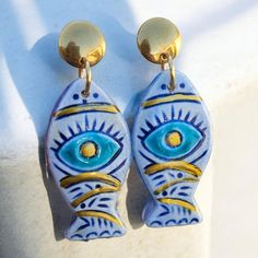 Enhance your jewelry collection with our unique Dangle Fish-Shaped Evil Eye Earrings. These striking earrings feature a handmade ceramic charm, intricately shaped like a fish and adorned with the iconic evil eye design. Each charm is crafted with care, ensuring that no two pieces are exactly alike, adding to their unique charm and character. The earrings are designed with a sturdy stainless steel stud, providing both durability and a sleek, modern look. Stainless steel is known for its hypoallergenic properties, making these earrings a great choice for those with sensitive ears. The fish-shaped evil eye charm is more than just a stylish accessory; it also carries a powerful symbolism of protection and good fortune. The dangle design adds a playful and elegant touch, making these earrings p Handmade Fish-shaped Earrings For Gifts, Blue Fish-shaped Earrings For Gift, Earrings Ceramic, Fish Earrings, Evil Eye Design, Earring Dangle, Evil Eye Earrings, Ceramic Earring, Fish Shapes