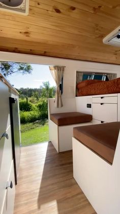 the inside of a camper with wood flooring and white cabinets, including a bed