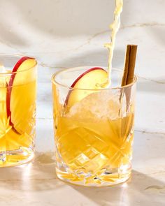 an apple cider being poured into two glasses filled with ice and apples on the side