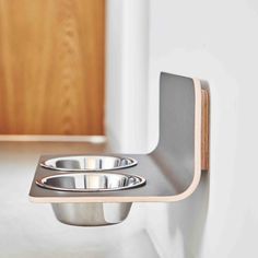 two stainless steel bowls sitting on top of a wooden shelf next to a white wall