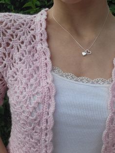 a woman wearing a pink cardigan with a heart pendant