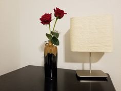 a vase with two roses in it sitting on a black table next to a lamp