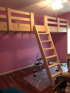 a loft bed with a ladder in the middle of it and purple walls behind it