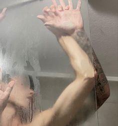 a man with his hands up in front of a mirror that has water on it