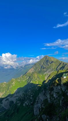 the mountains are covered in green grass and blue skies with clouds above them, as well as some rocks below