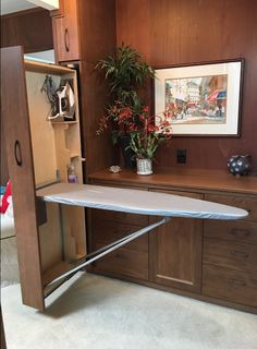 an ironing board sits in the corner of a room with wooden cabinets and drawers