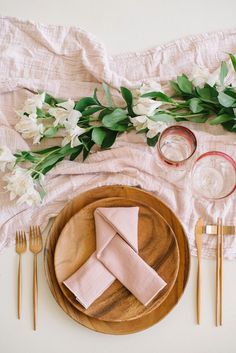 the table is set with pink napkins, goldware and white flowers on it