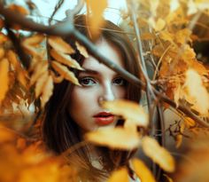 a woman with blue eyes standing in front of leaves and branches, looking at the camera