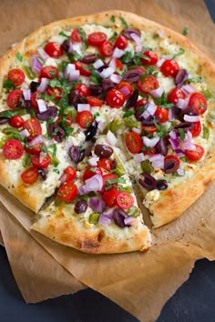 a pizza with tomatoes, onions and other toppings on it sitting on a piece of wax paper