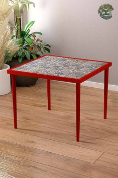 a red table sitting on top of a hard wood floor next to a potted plant