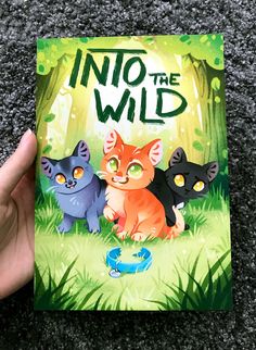 a hand holding up a book with three cats in the wild on it's cover